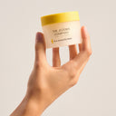 Hand holding a jar of 'The Jojoba Company' Pure Jojoba Gel Mask against a plain background