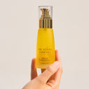 Hand holding a yellow bottle labeled  Ultimate Youth Potion from 'The Jojoba Company' against a beige background