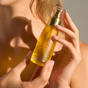 Model holding a bottle of Ultimate Youth Potion from The Jojoba Company skincare product with a warm glow.