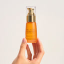 Hand holding a bottle of Vitamin C Glow Potion from The Jojoba Company product against a light background