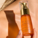 Vitamin C Glow Potion serum bottle from The Jojoba Company with gold cap held against a skin-toned background